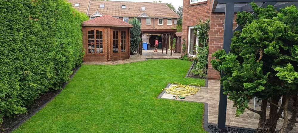 Ein gepflegter Hinterhof mit einem üppigen grünen Rasen, einem hölzernen Pavillon und einem Backsteinhaus im Hintergrund.
