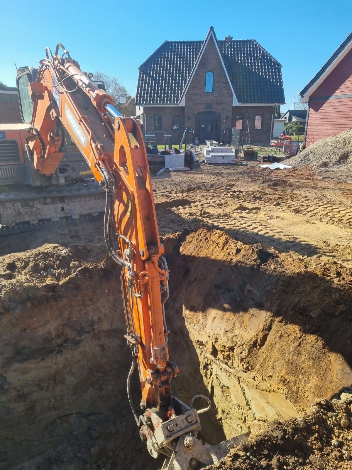Ein orangefarbener Bagger gräbt vor einem Haus ein Loch in die Erde.