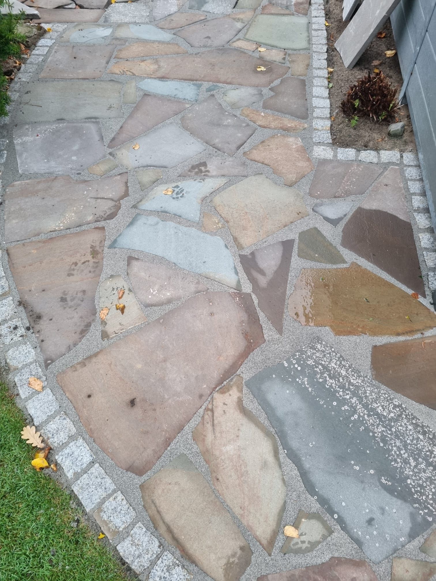 Plattenweg mit grauer Umrandung, Steine in verschiedenen Erdtönen, im Freien.