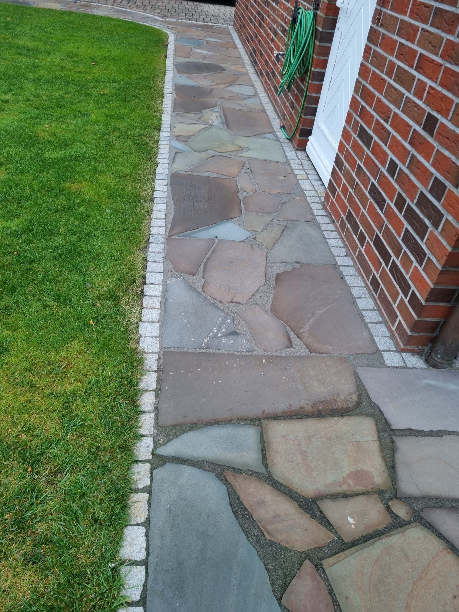 Steinweg neben Rasen und Backsteingebäude.