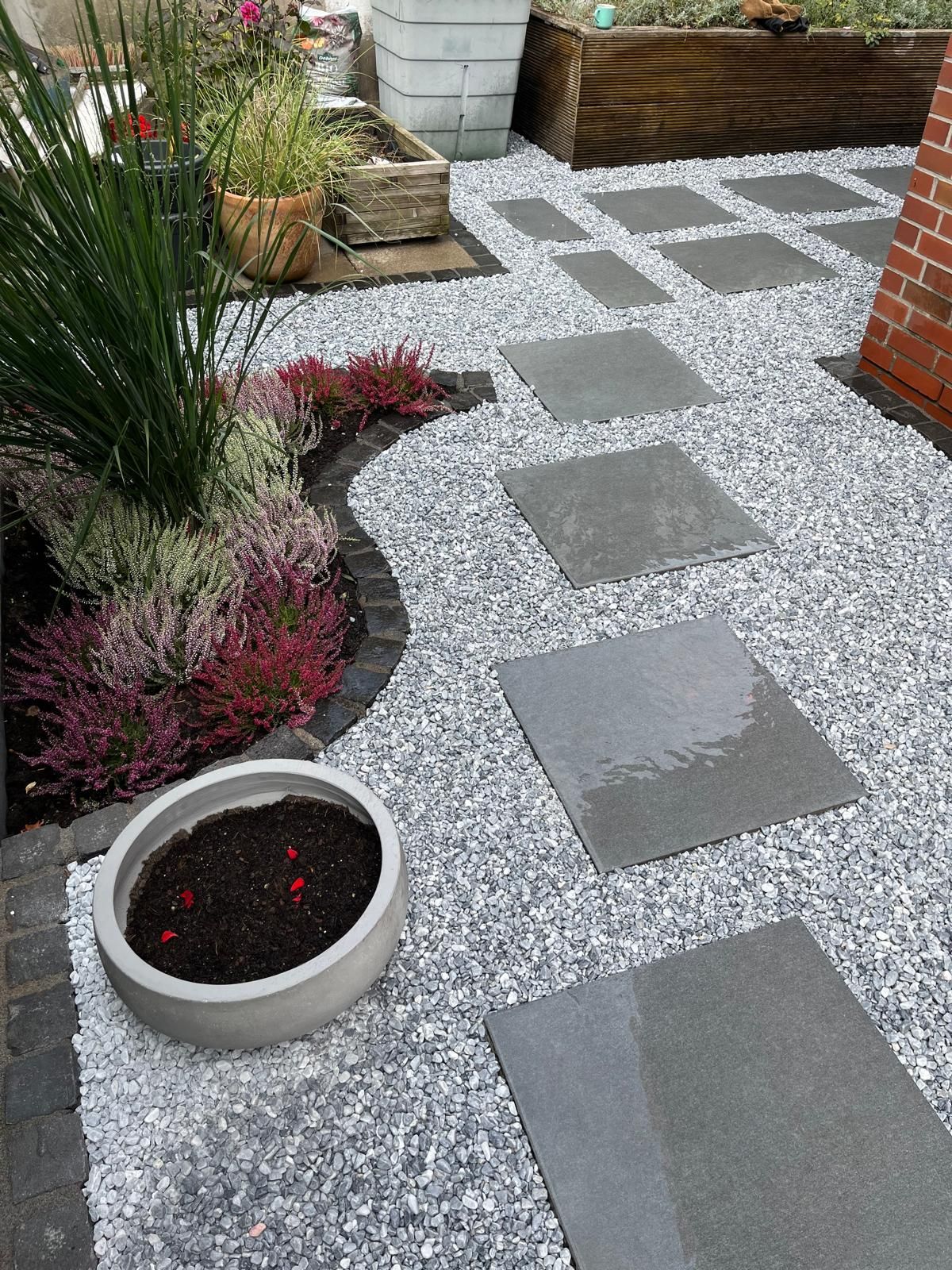 Steinweg mit Trittsteinen, Kies und einem Gartenbeet mit lila und grünen Pflanzen.