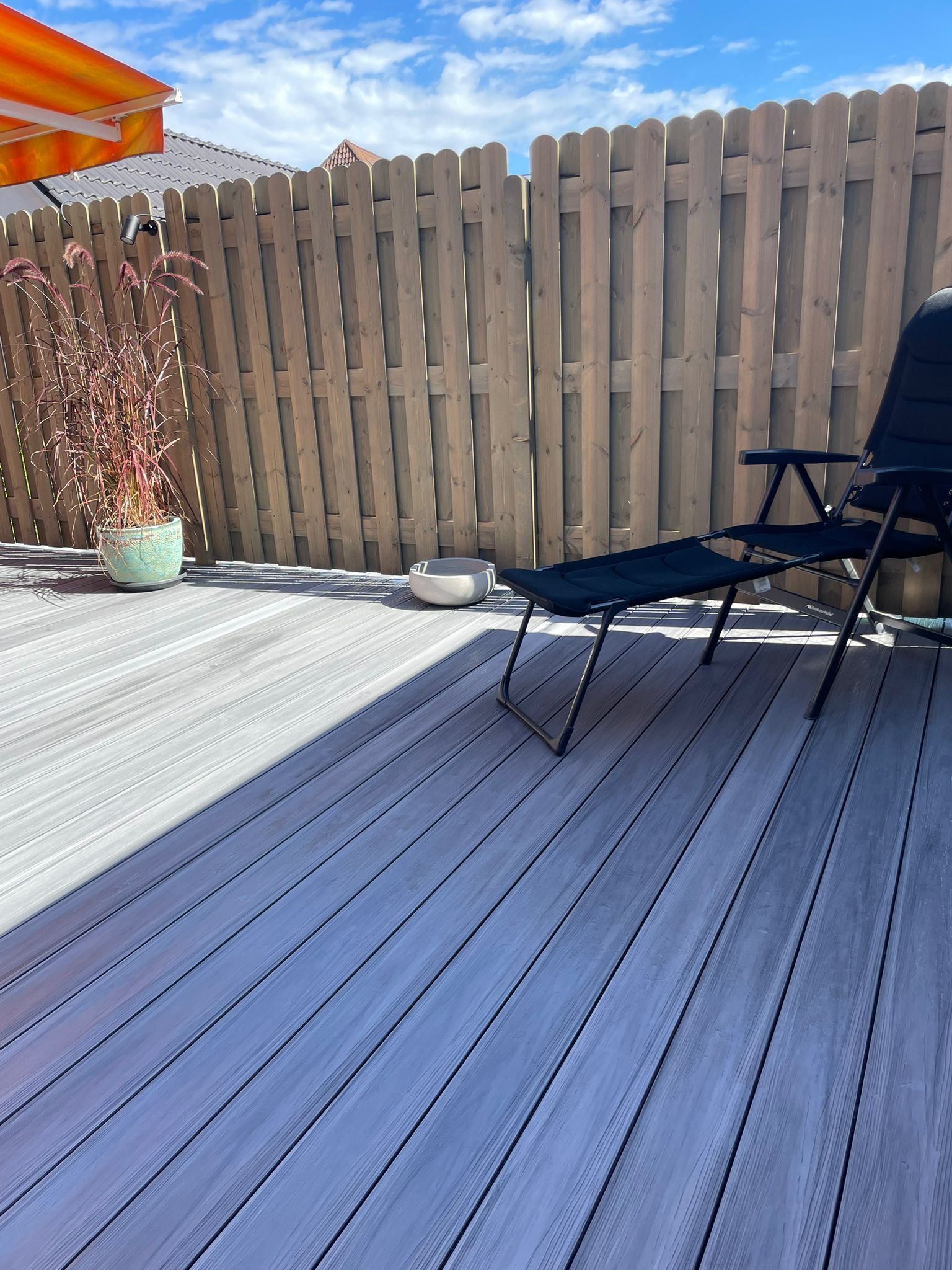 Eine Terrasse mit Stuhl, Pflanze und Holzzaun an einem sonnigen Tag.