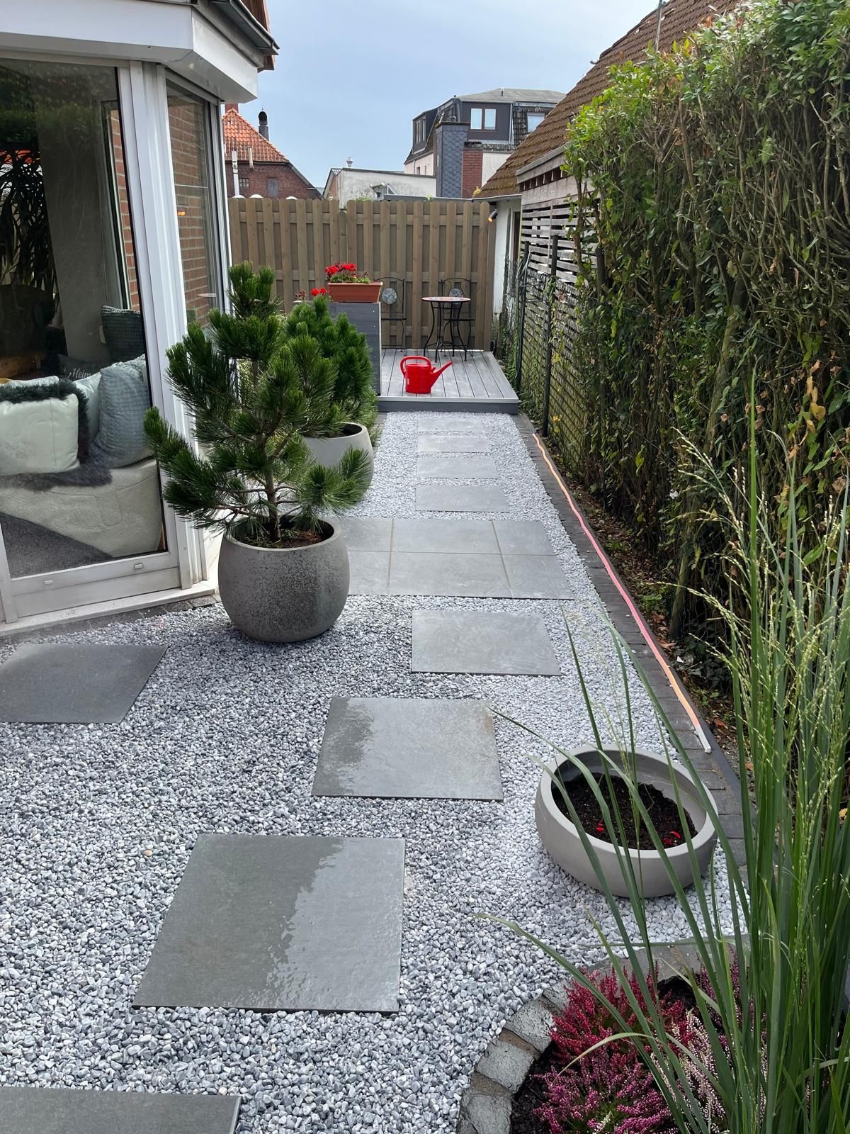 Steinweg durch einen Garten mit Topfpflanzen und Kies.