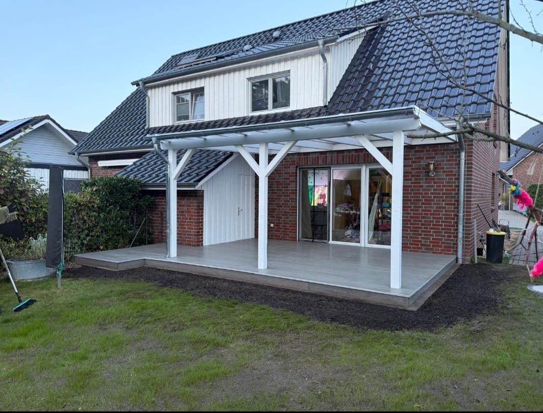 Hinterhofterrasse mit weißer Pergola, Backsteinhaus und grünem Rasen.