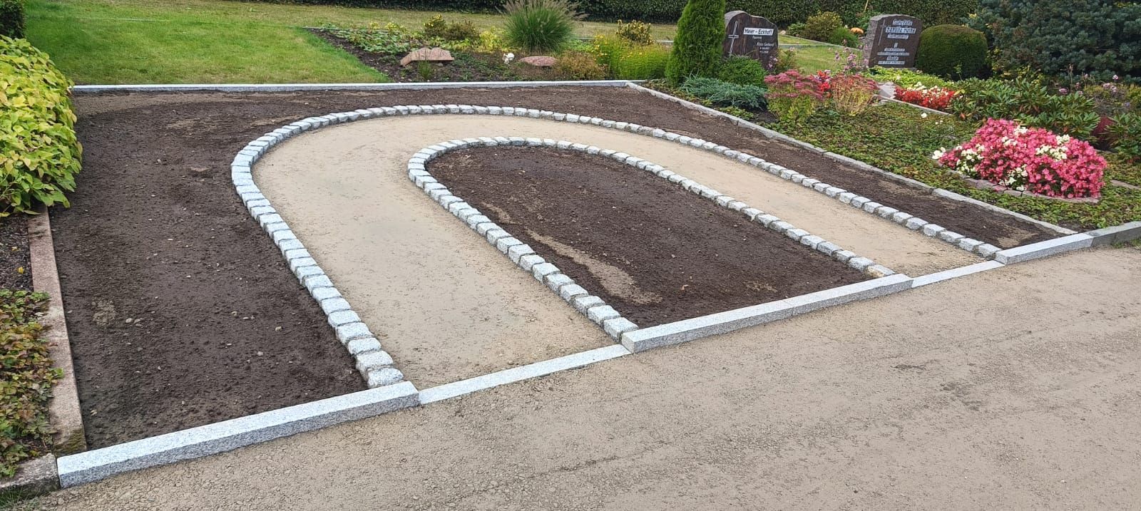 Eine Grabstätte mit einem U-förmigen, mit Steinen gesäumten Weg; Erde befindet sich in der Mitte und an den Seiten.