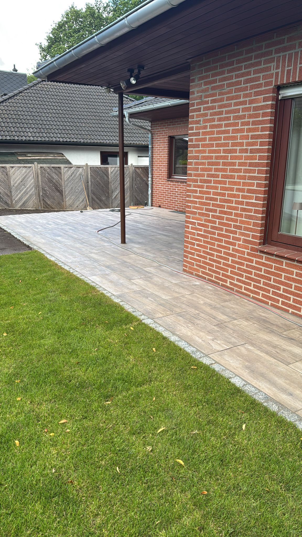 Hausfassade aus Backstein mit Holzterrasse und grünem Rasen.