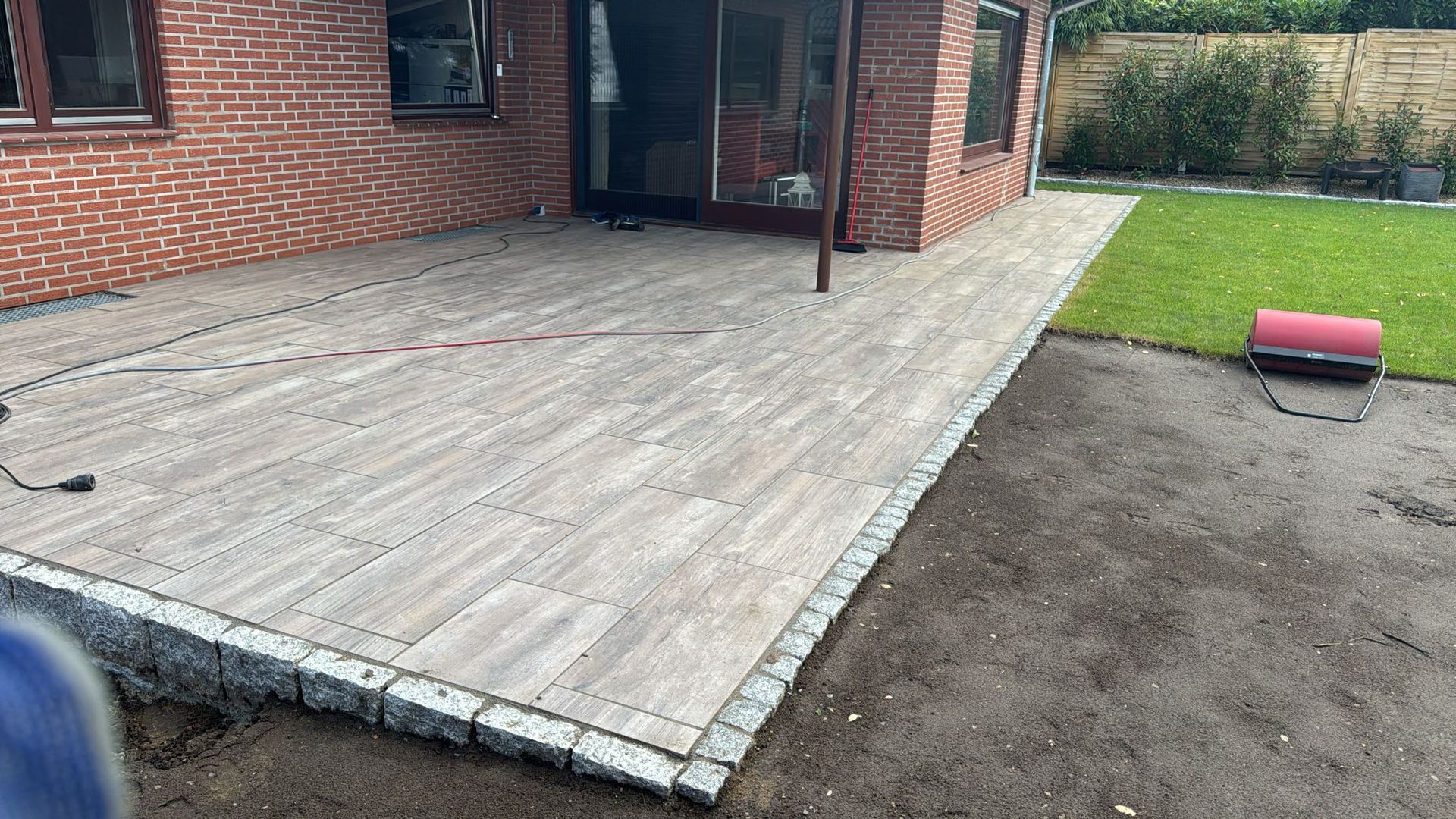 Backsteinhaus mit neu gepflasterter Terrasse, die von grauen Steinen eingefasst ist und zu einem Rasen führt.