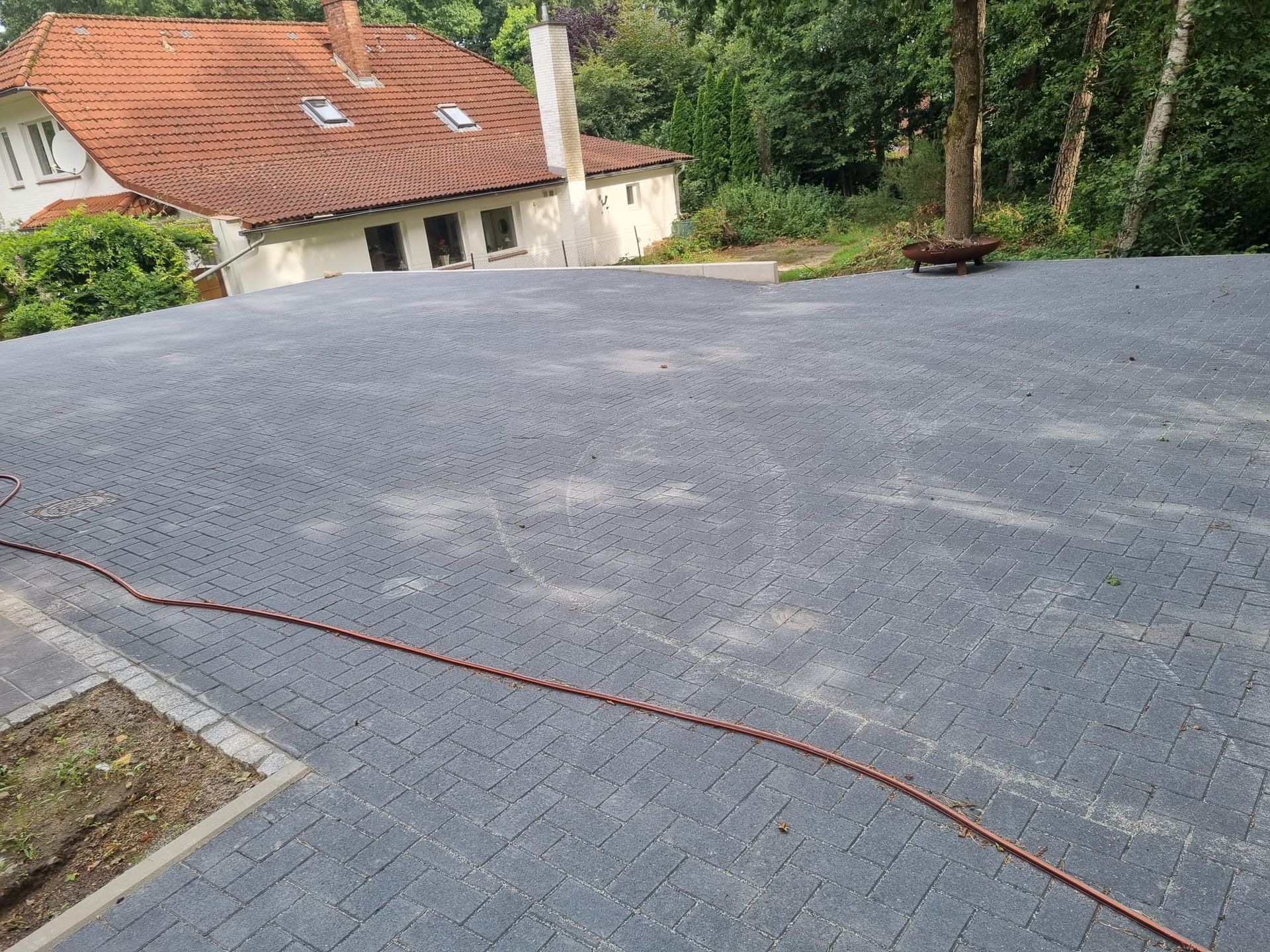 Grau geflieste Terrasse mit Haus im Hintergrund und Bäumen auf der rechten Seite.