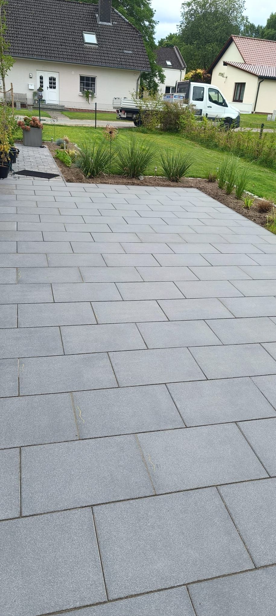 Ein grauer, gepflasterter Gehweg führt zu einem grünen Schuppen zwischen zwei Häusern mit grünem Rasen.