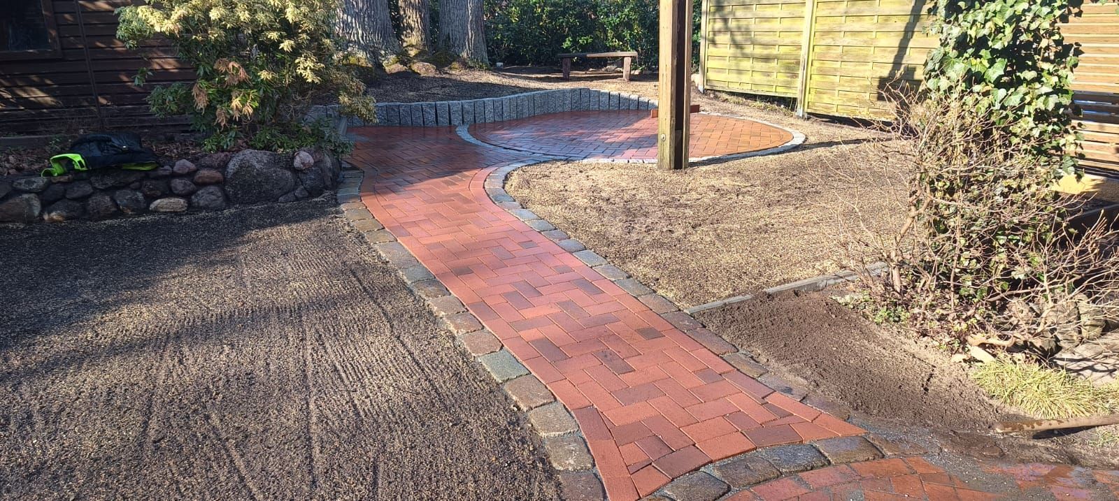 Ein gemauerter Weg, der zu einem Holzzaun in einem Garten führt.