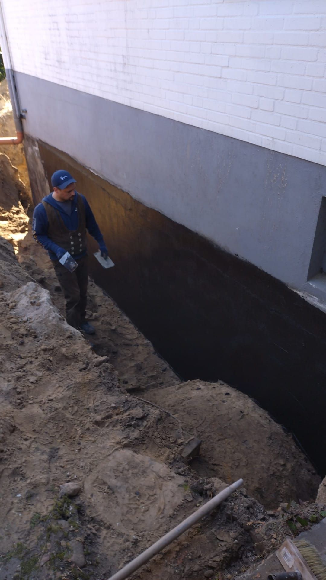 Ein Mann steht mit einer Schaufel in der Hand neben einer Mauer.