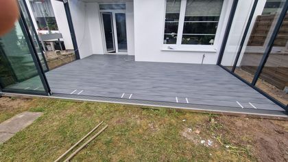 Vor einem Haus mit vielen Fenstern wird eine Terrasse gebaut.