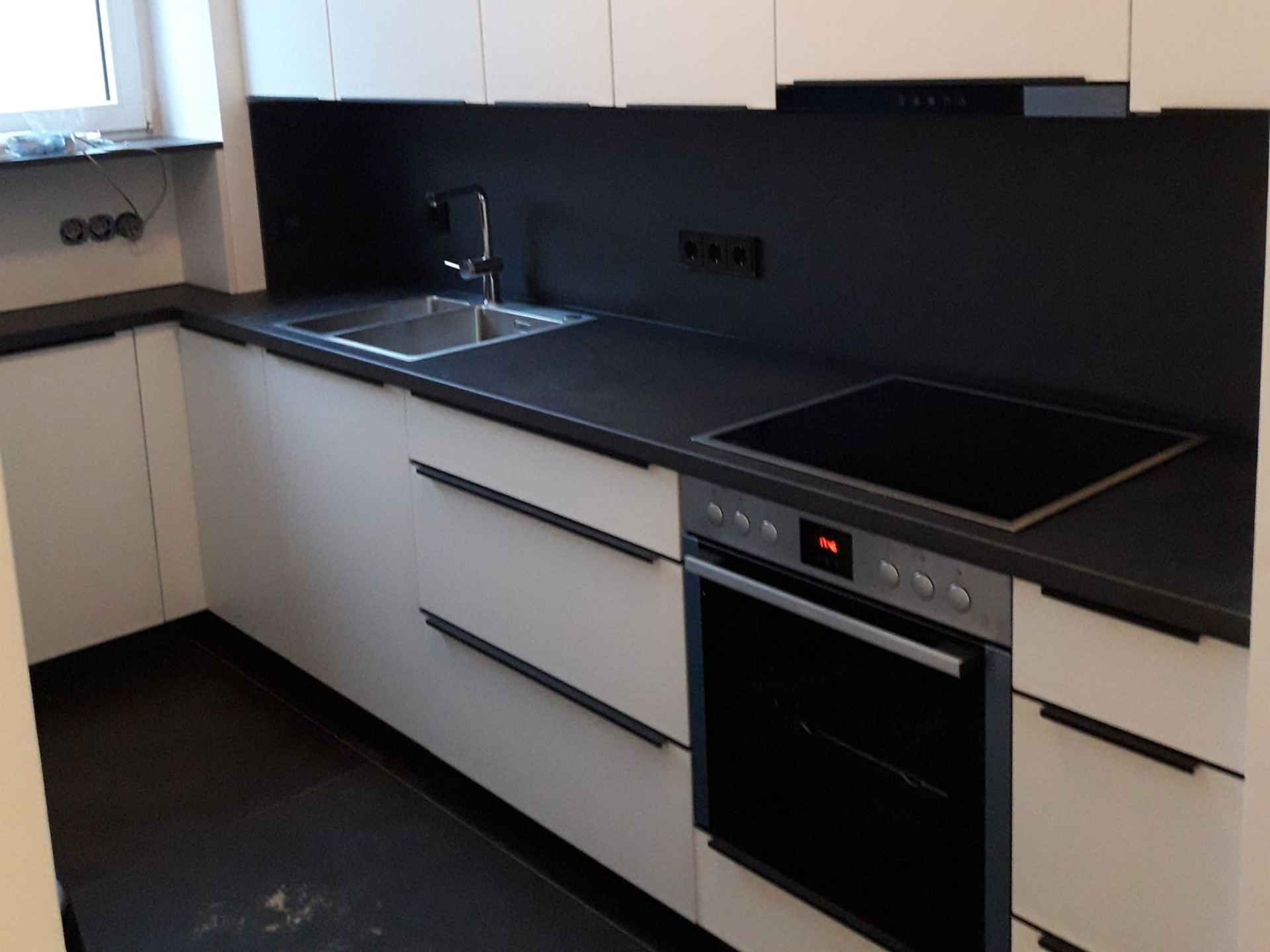 Moderne Küche mit weißen Schränken, dunklen Arbeitsplatten und Einbaugeräten.