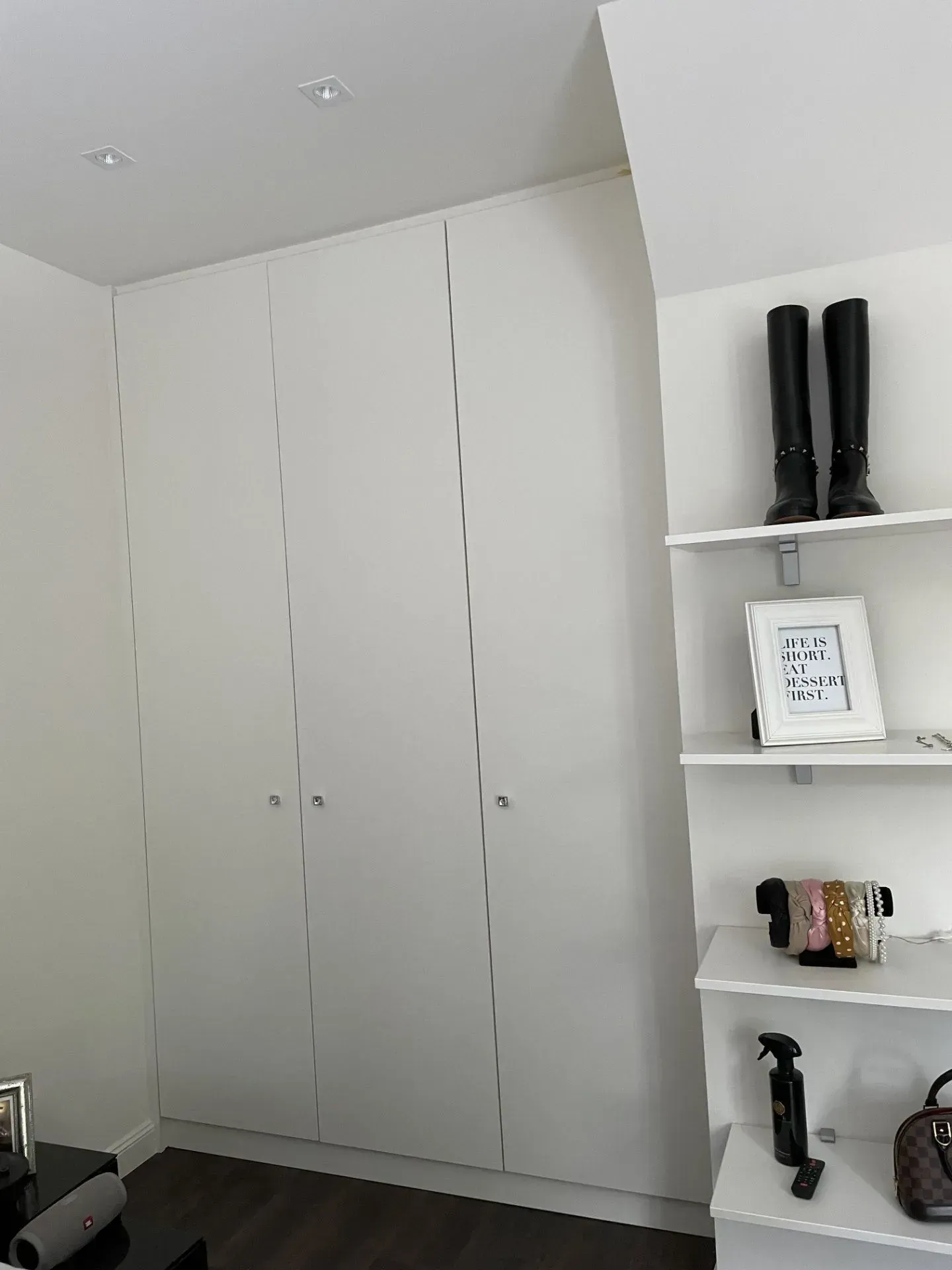 Weißer Kleiderschrank mit geschlossenen Türen, Regale auf der rechten Seite mit Stiefeln, Bilderrahmen und Taschen.