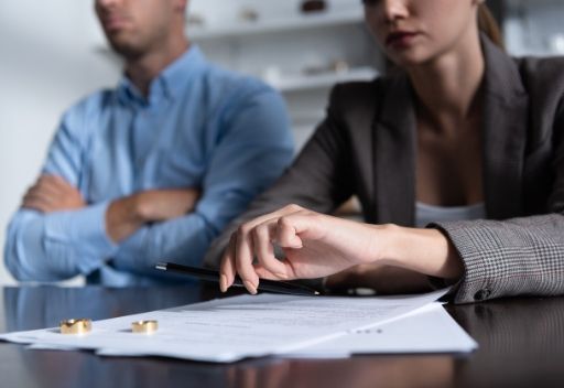Un hombre y una mujer están sentados en una mesa con papeles y anillos de boda encima.
