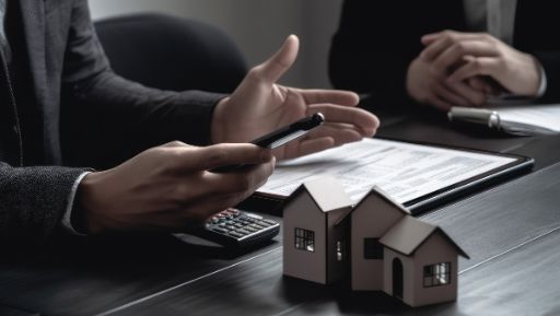 Dos hombres están sentados en una mesa con casas en miniatura y una calculadora.