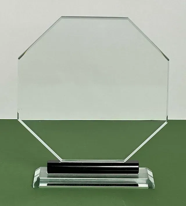 Un trofeo de cristal transparente con una base negra está sobre una mesa verde.