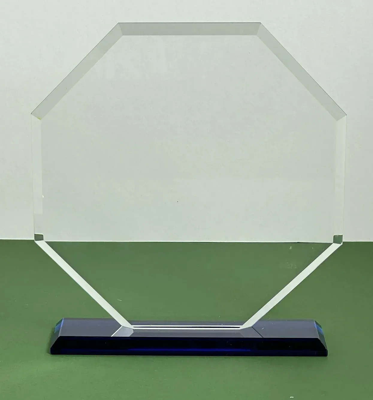 Un trofeo de cristal transparente con una base azul está sobre una mesa verde.