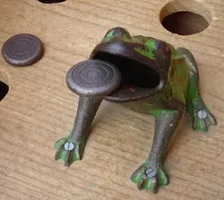 Una rana con una moneda en la boca está sentada en una mesa de madera.