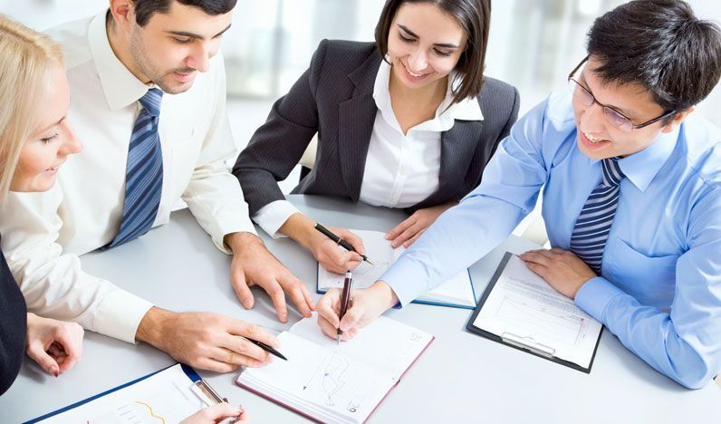 Un grupo de personas están sentadas alrededor de una mesa escribiendo en cuadernos.