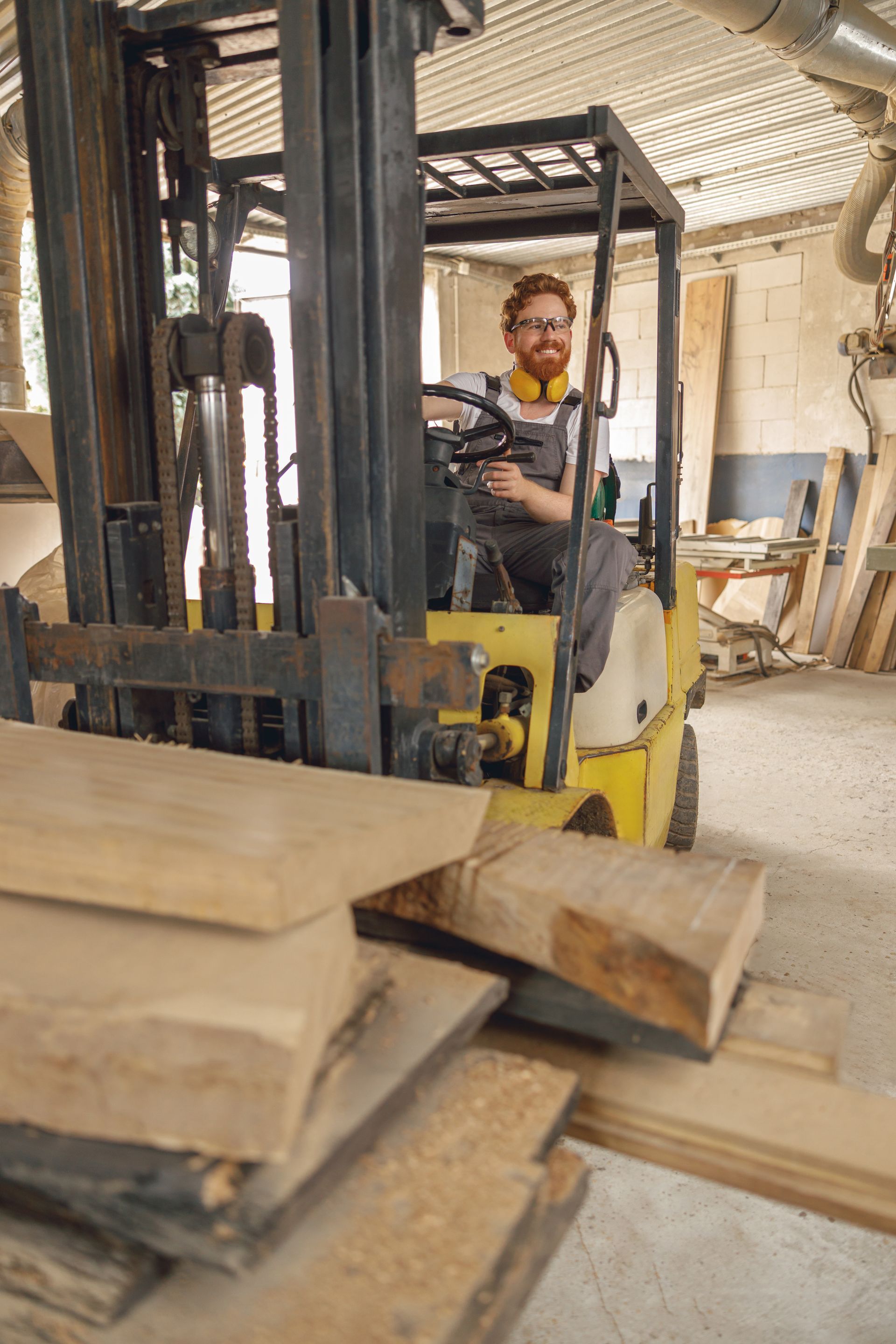 Un homme conduit un chariot élévateur jaune, transportant du bois dans un atelier.