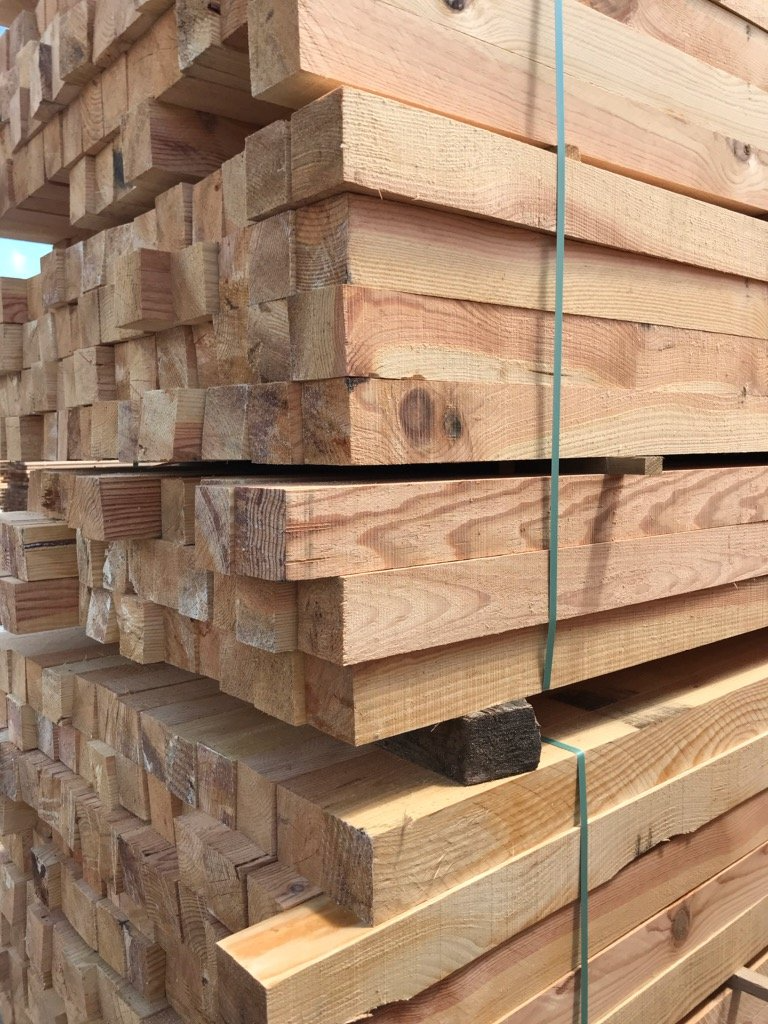 Pile de bois fraîchement coupé, liée par des sangles vertes.