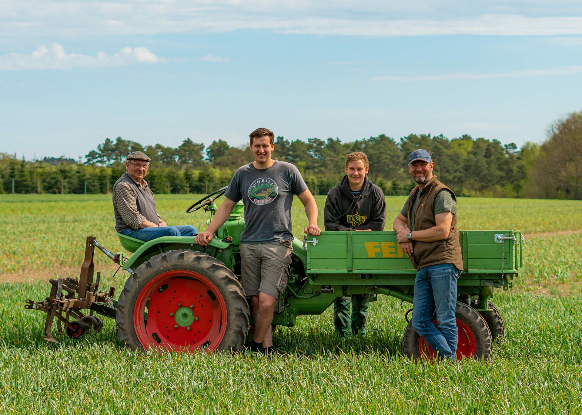 Eine Gruppe von Menschen steht neben einem grünen Traktor auf einem Feld.