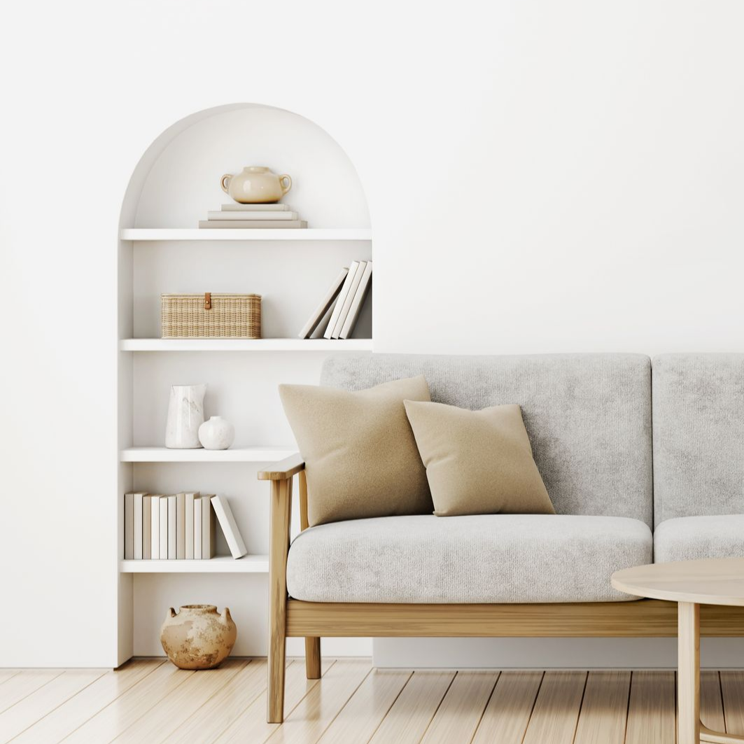Salon minimaliste avec canapé beige, étagères blanches cintrées et décoration tissée dans un espace blanc lumineux