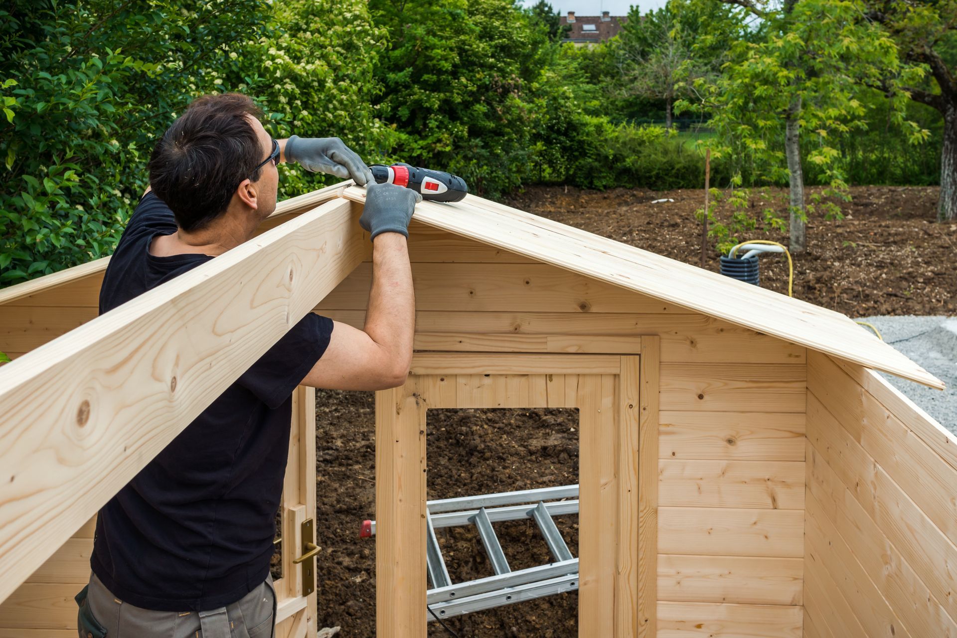 Un ouvrier en train d'installer le toit en bois d'un abri dans un jardin.
