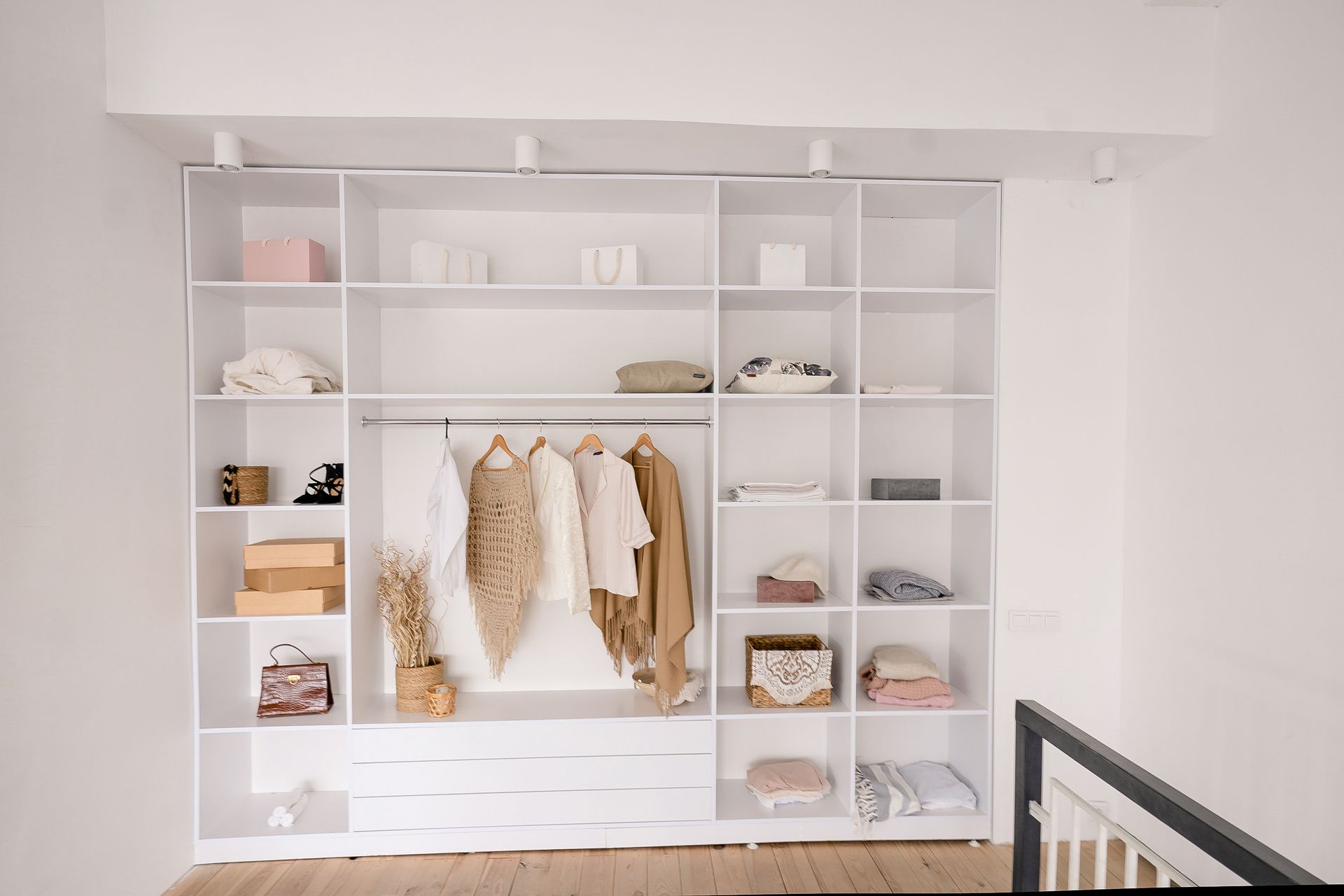 Placard blanc minimaliste avec étagères, tiroirs et vêtements suspendus dans une chambre lumineuse.