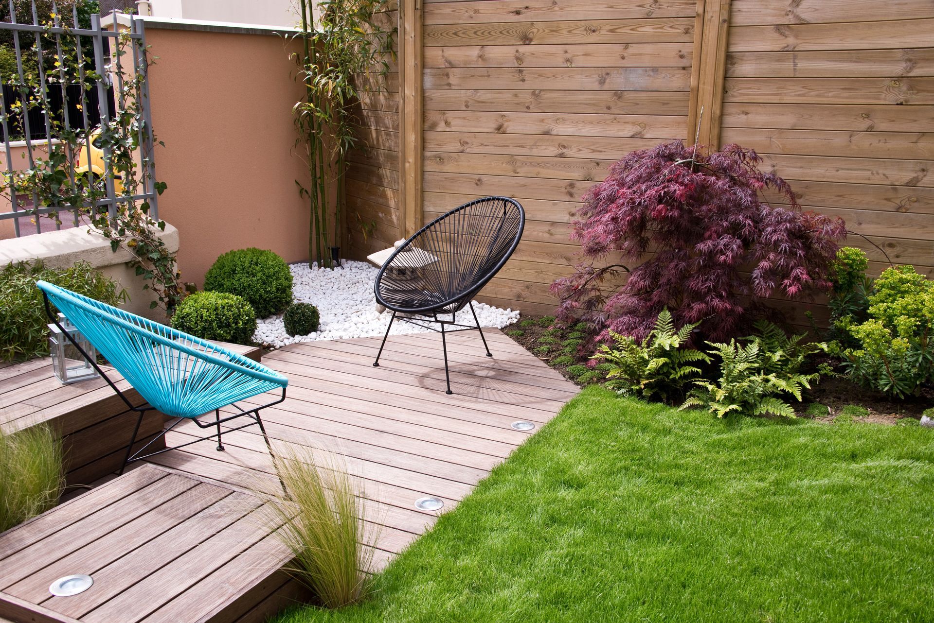 Terrasse arrière avec deux chaises longues, une petite table et un arbuste violet au bord d'une pelouse verte.