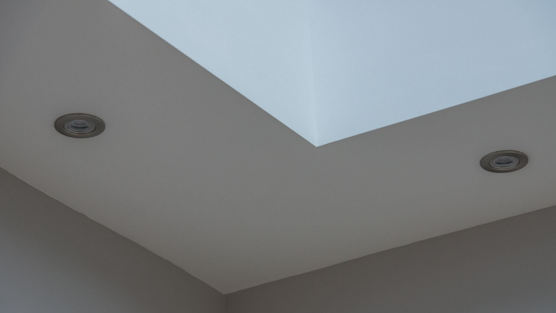 Coin de plafond avec spots encastrés et puits de lumière dans une pièce blanche