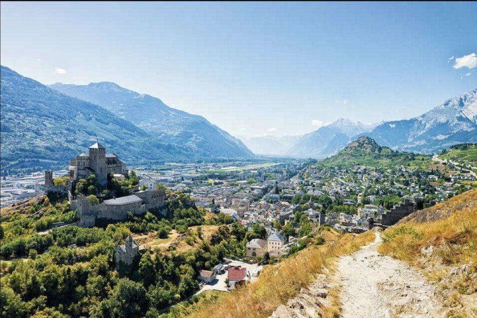 Un château se trouve au sommet d'une colline surplombant une ville dans les montagnes.