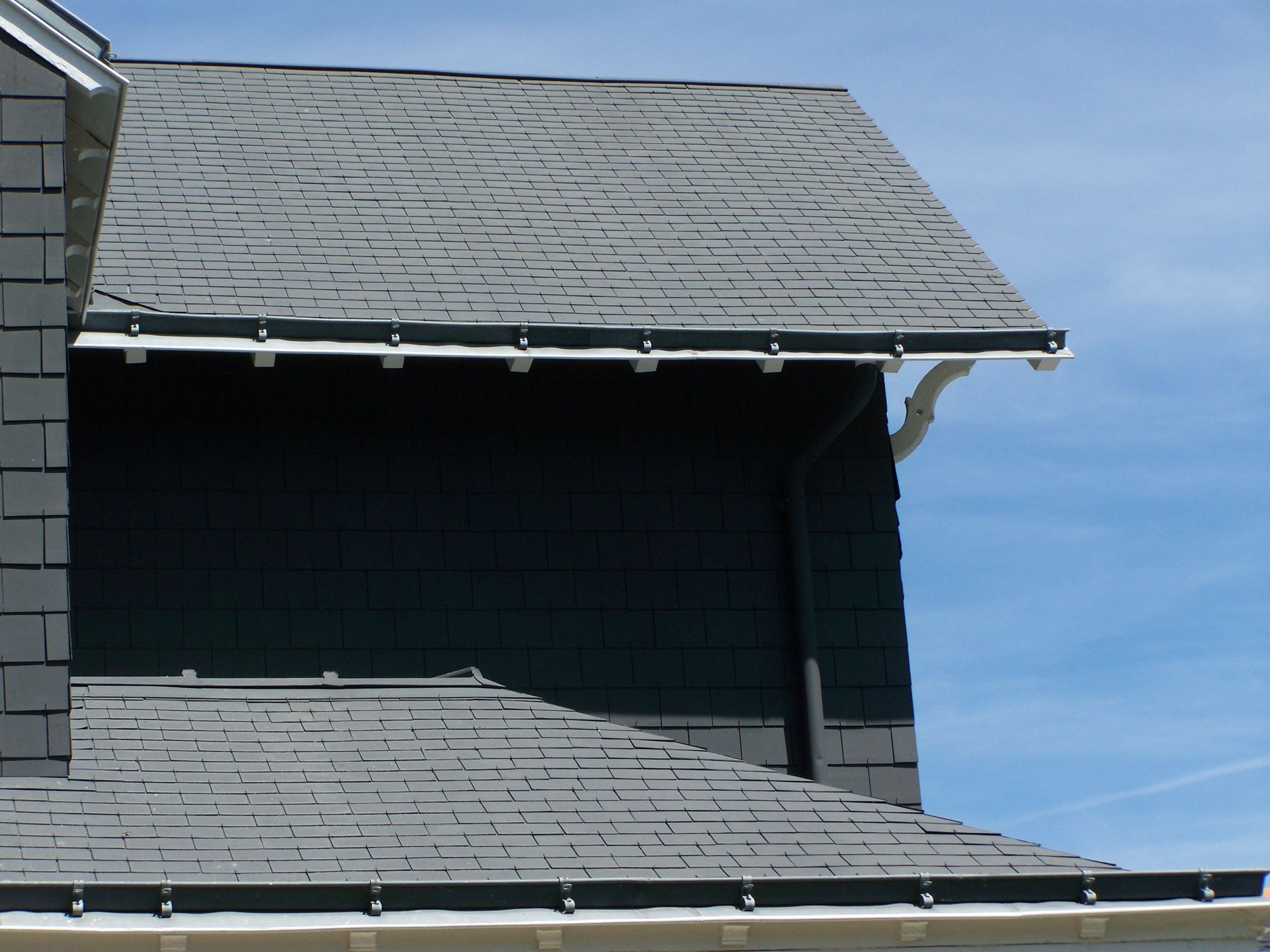 Un couvreur portant des gants installe des tuiles en terre cuite orange sur une charpente de toit en bois recouverte d'une bâche de protection noire.