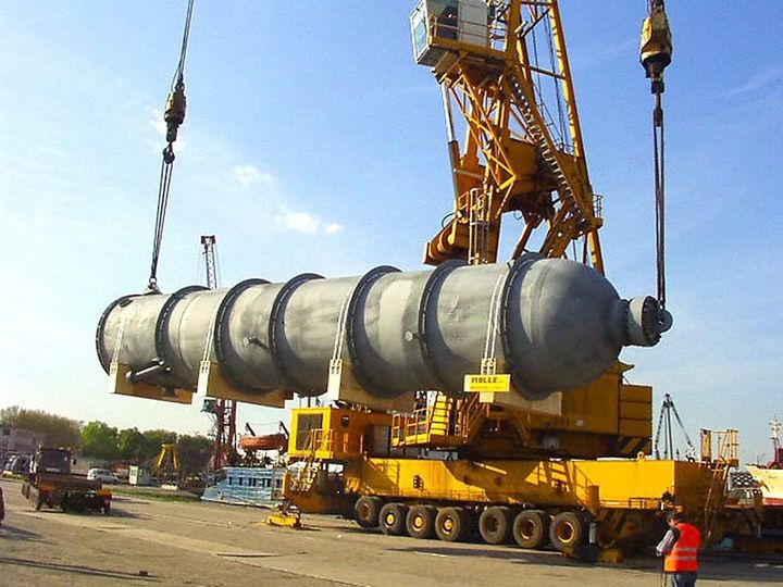Large industrial cylinder lifted by a yellow crane at a construction site under a blue sky