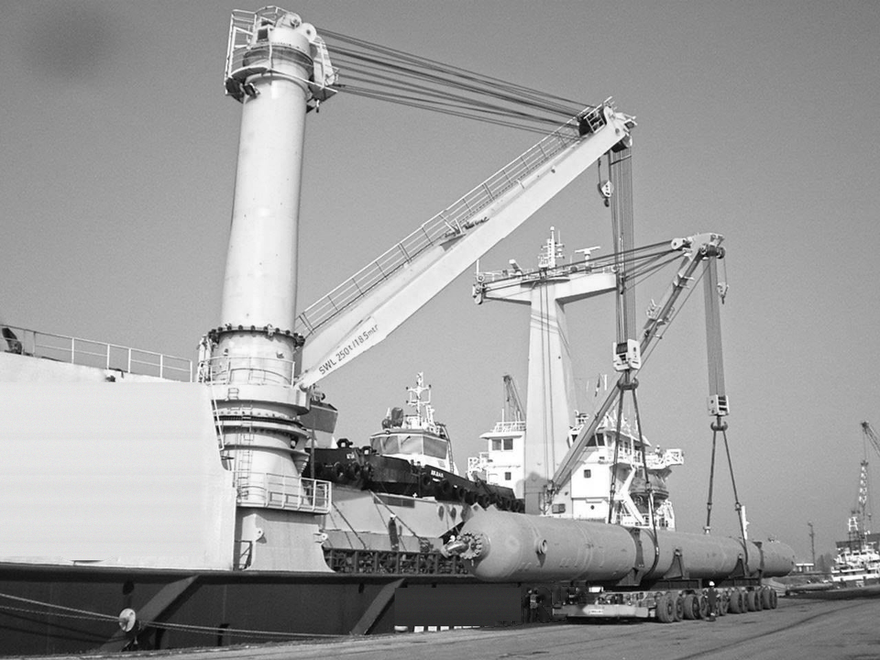 Cargo ship under construction at a shipyard, with cranes lifting large steel sections along the hull.
