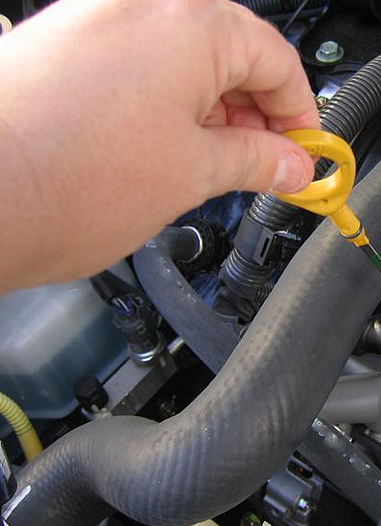 Main retirant la jauge d'huile jaune du moteur de la voiture.