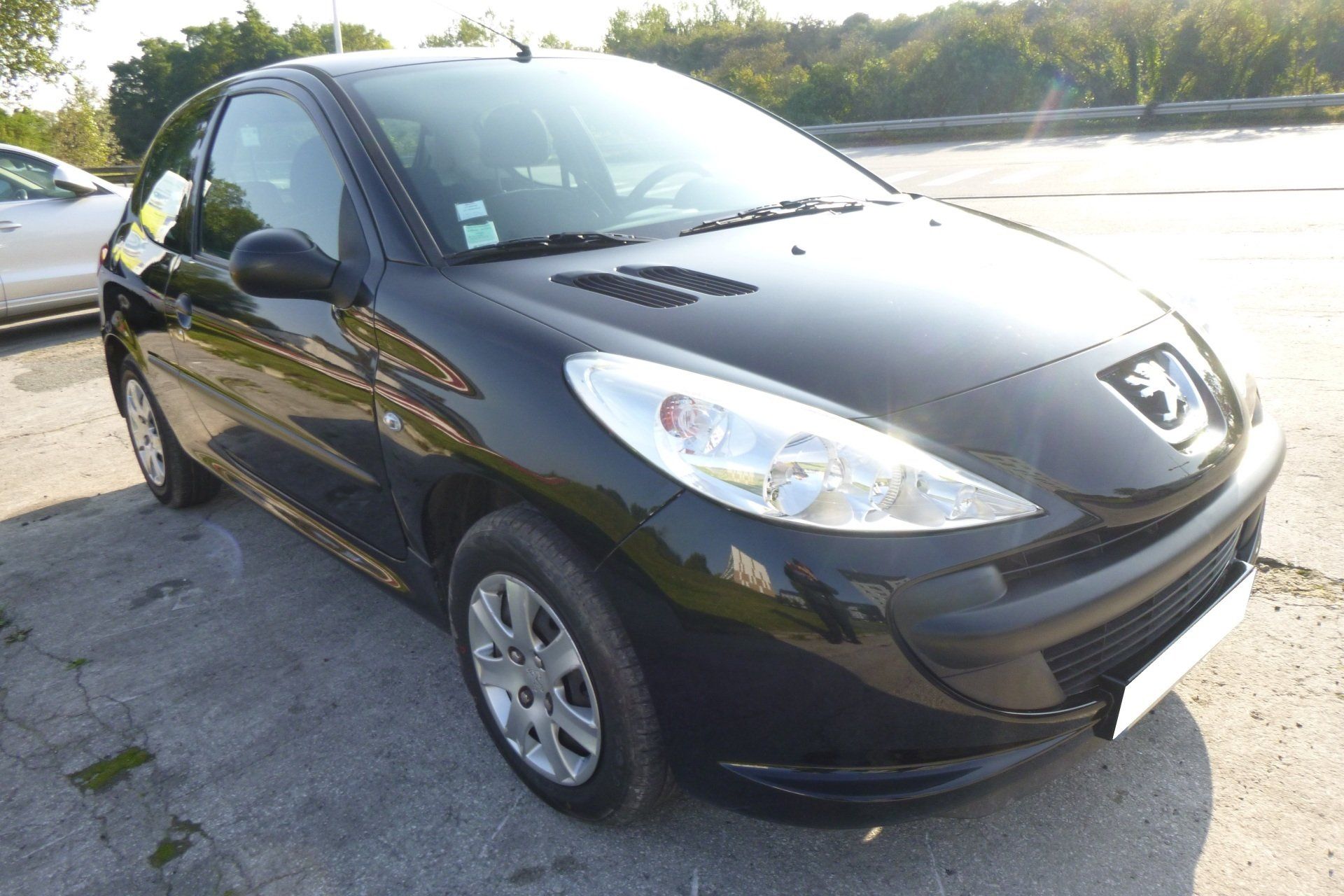 Peugeot 206 noire garée sur du béton, journée ensoleillée.