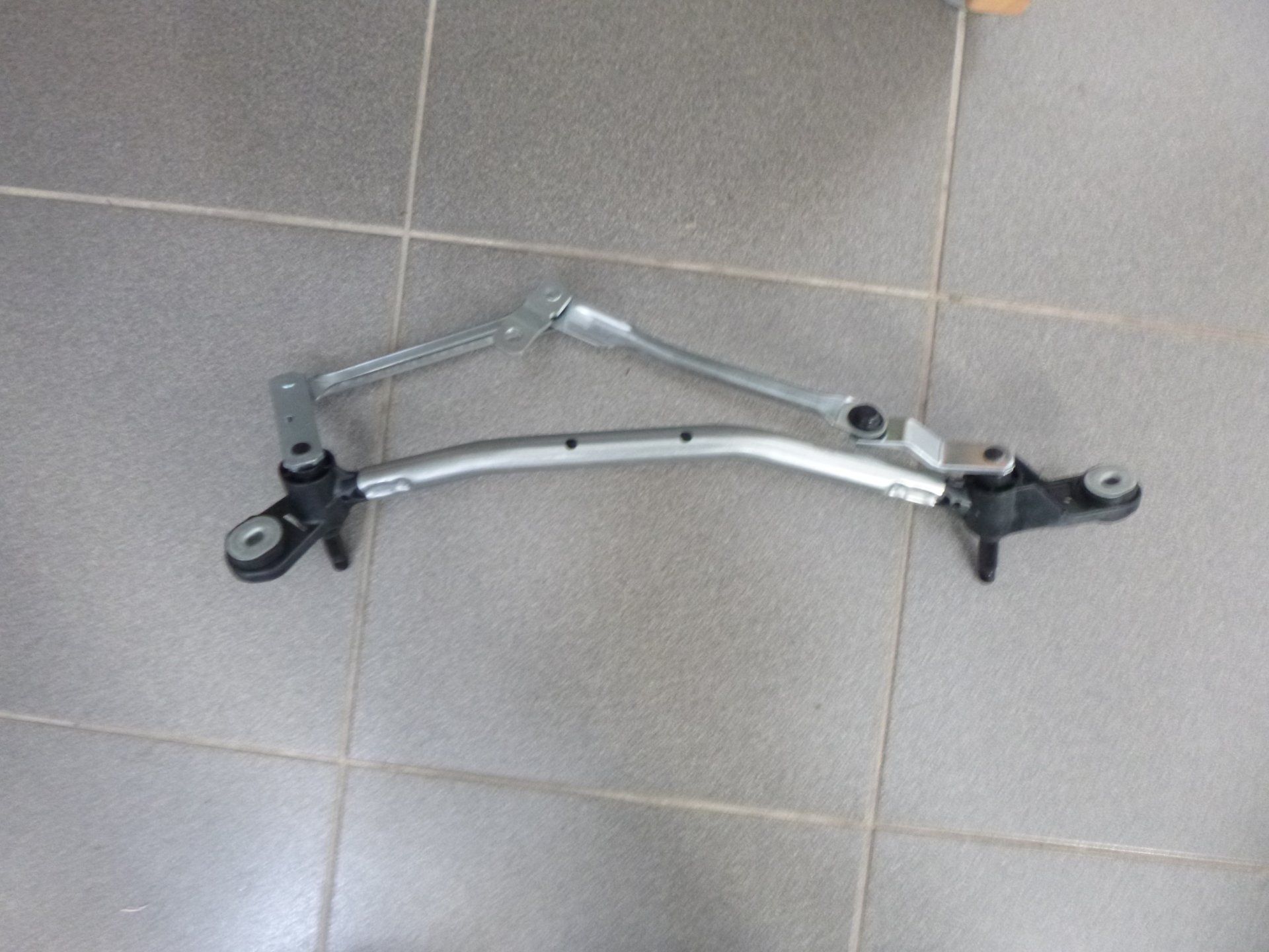 Ensemble de tringlerie d'essuie-glace argenté sur un sol carrelé.