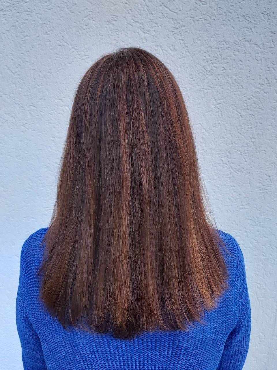 Eine Frau mit langen braunen Haaren trägt einen blauen Pullover. BM Hair and Beauty