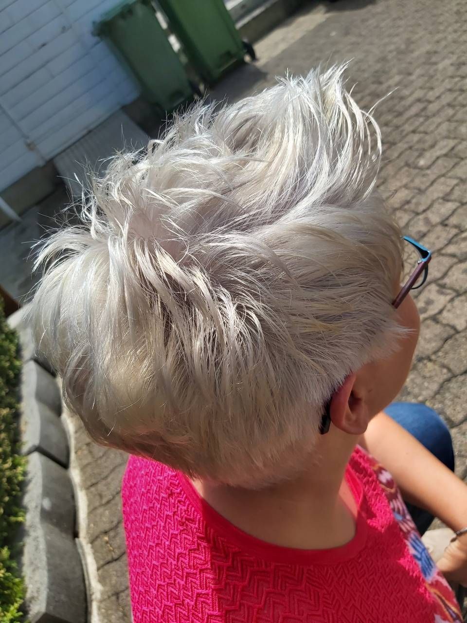 Eine Frau mit weißem Haar und Brille trägt ein rosa Hemd. BM Hair and Beauty