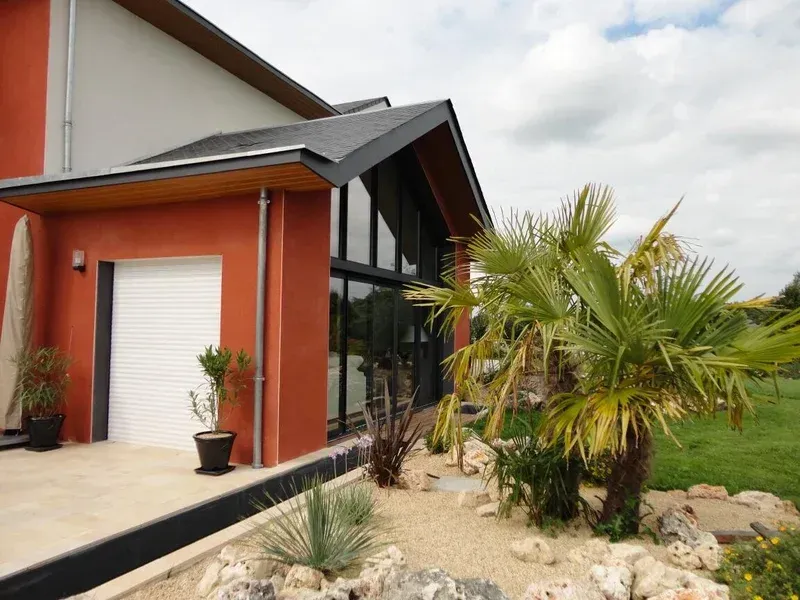 Bâtiment moderne avec façade orange, de grandes fenêtres et d'aménagement paysager avec des palmiers.