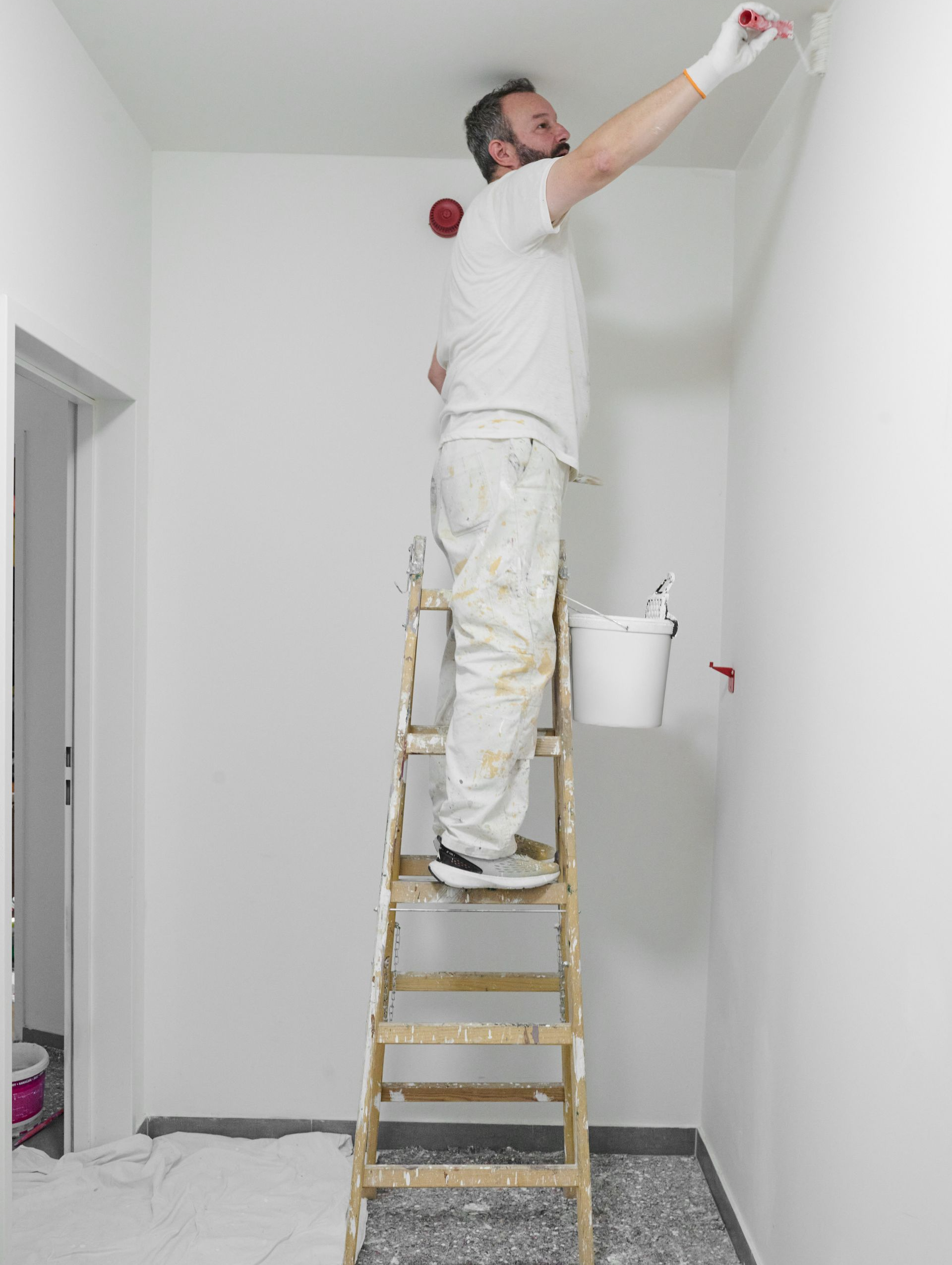 Un homme sur un escabeau tient un rouleau de peinture appliqué sur un mur