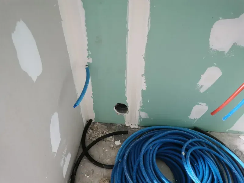 Vue intérieure d'une cloison sèche avec la plomberie. Tuyaux bleus et rouges, et tubes noirs au sol.