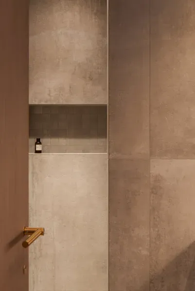 Salle de bains moderne avec carrelage gris, une étagère encastrée supportant une bouteille et une poignée dorée.