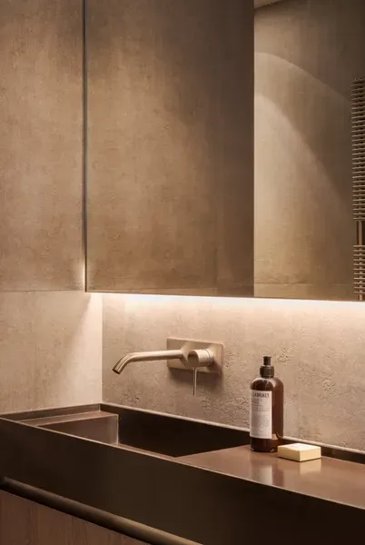 Lavabo de salle de bains moderne avec un robinet en bronze et un savon, sous un miroir. Éclairage chaleureux et couleurs douces.