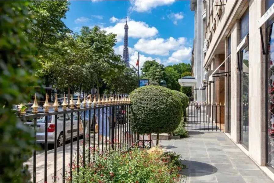 Vue de la tour Eiffel depuis une rue de Paris, à travers une grille en fer forgé et des arbres.