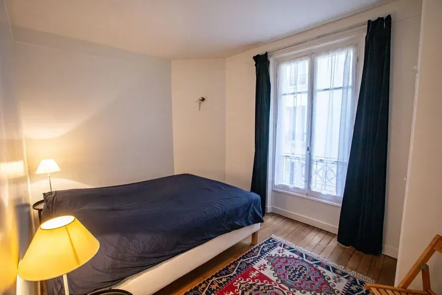 Chambre avec un lit, une fenêtre avec des rideaux, un tapis et une lampe.