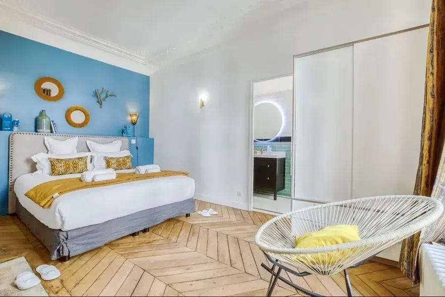 Chambre avec lit, mur bleu, chaise et porte ouverte donnant sur une salle de bains.
