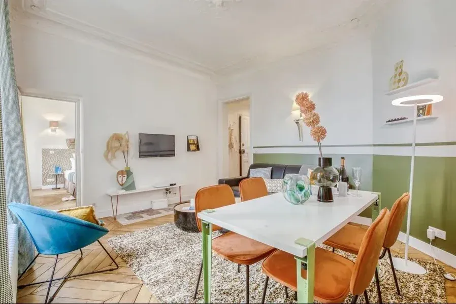 Salon avec table à manger et des chaises orange, canapé, télévision et des objets décoratifs.